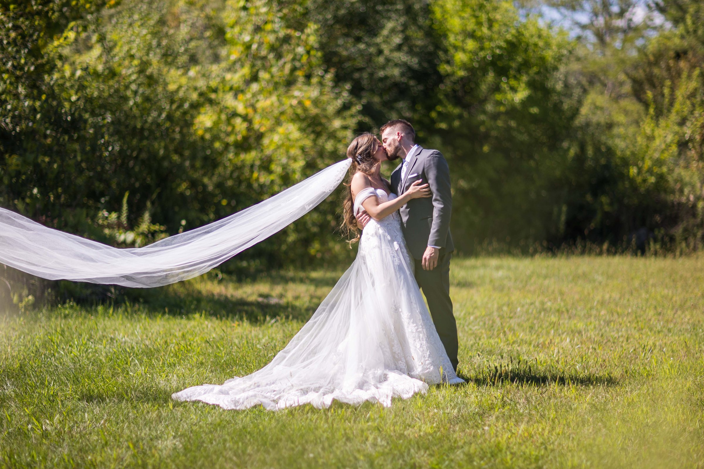Rebecca and Nick sharing a kiss outdoors with Rebecca's veil flowing behind them
