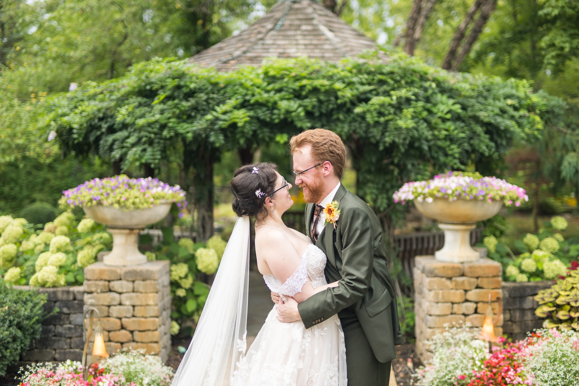 Persephone and Mark smiling together in the gardens on their wedding day