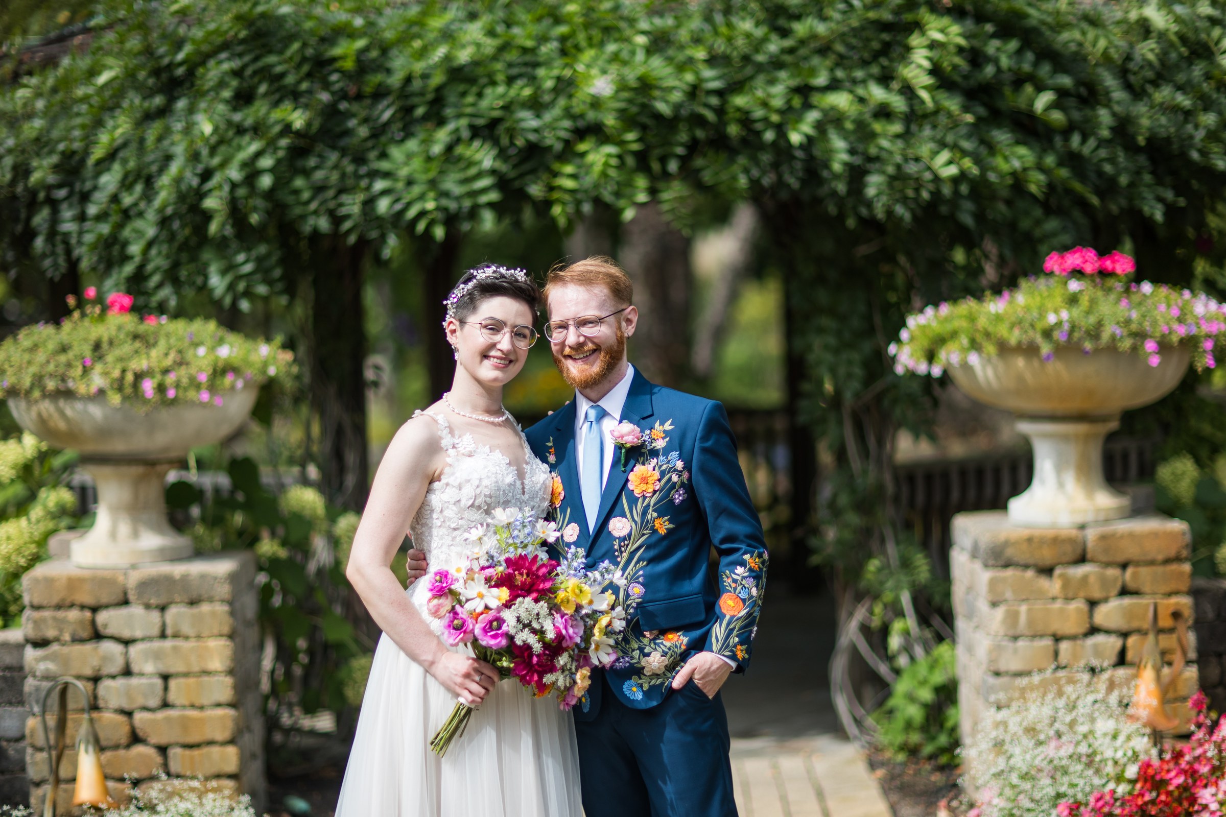 Rose and Ben smiling together beneath a garden arch on their wedding day